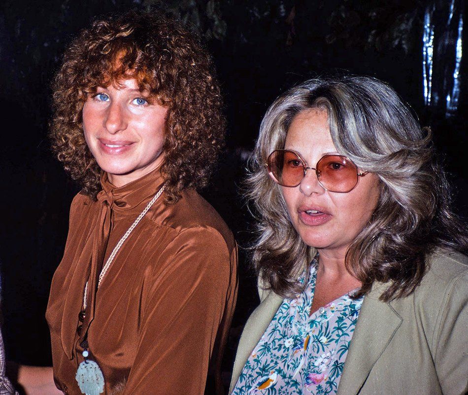 Photo of Barbra next to her agent, Sue Mengers. Barbra wears a rust colored top, and Mengers has on sunglasses.