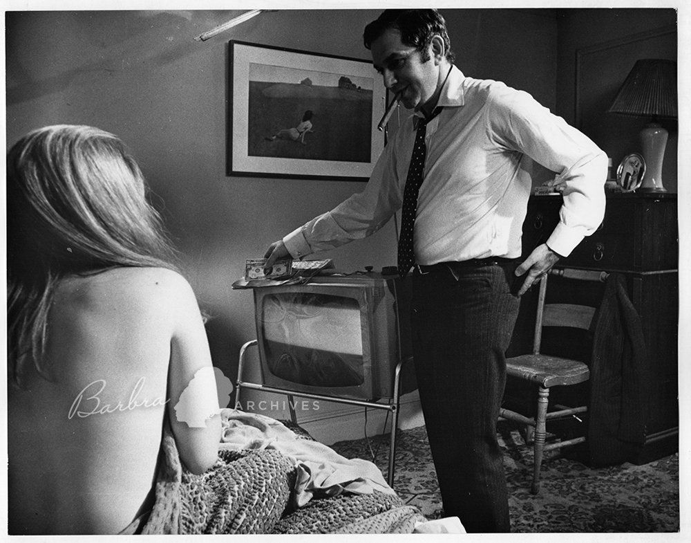 Man standing by a TV talking to a seated Streisand in a dim living room