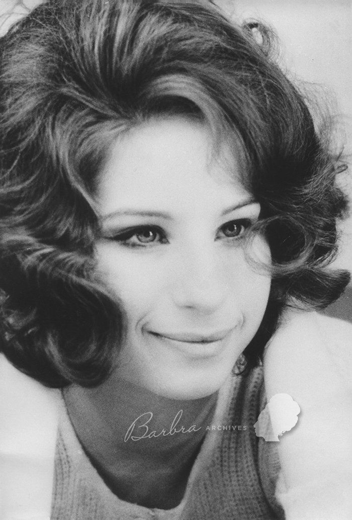 Black-and-white portrait of Barbra with voluminous curly hair, looking slightly to the side.