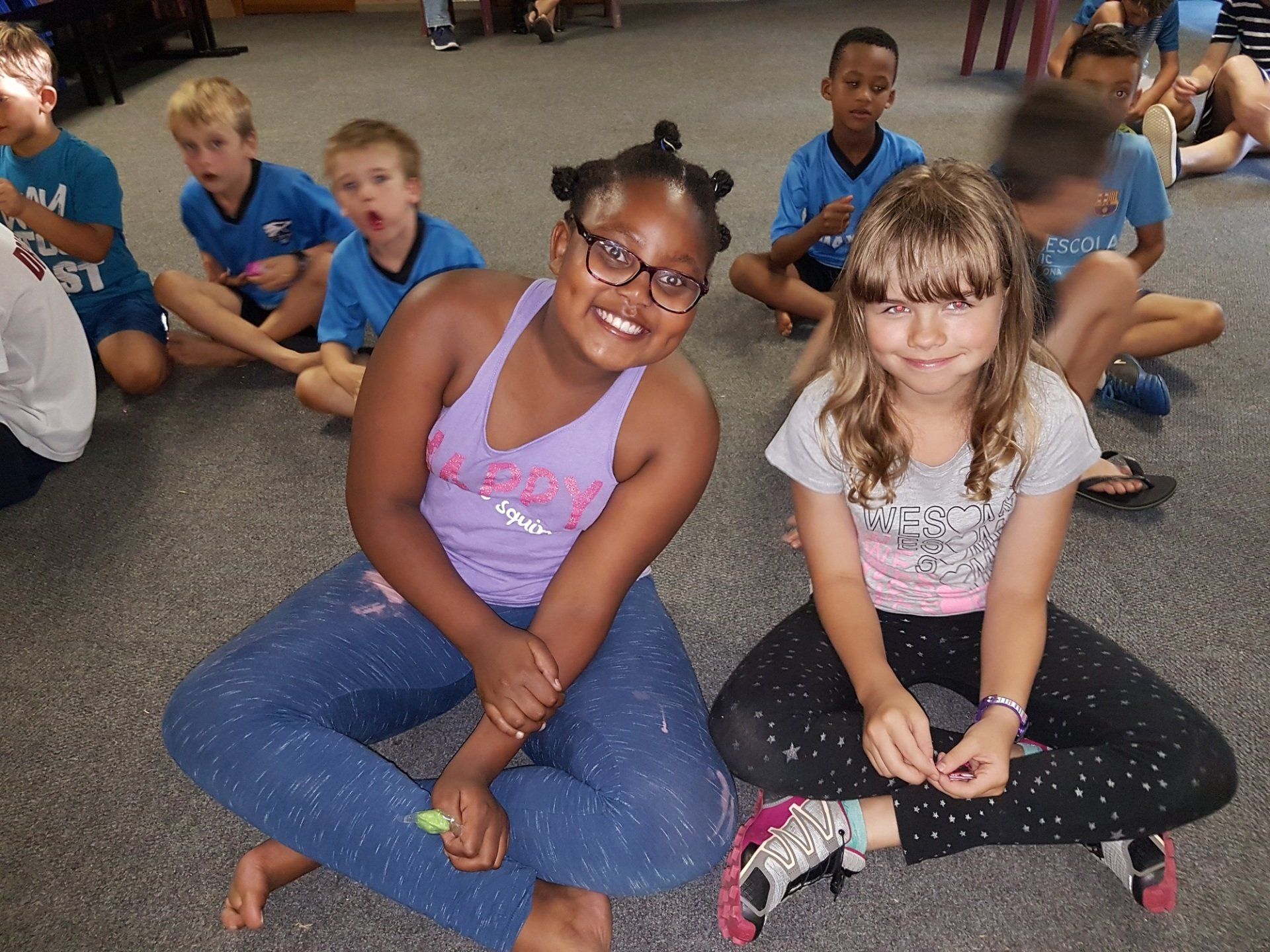 A girl in a purple tank top sits next to another girl