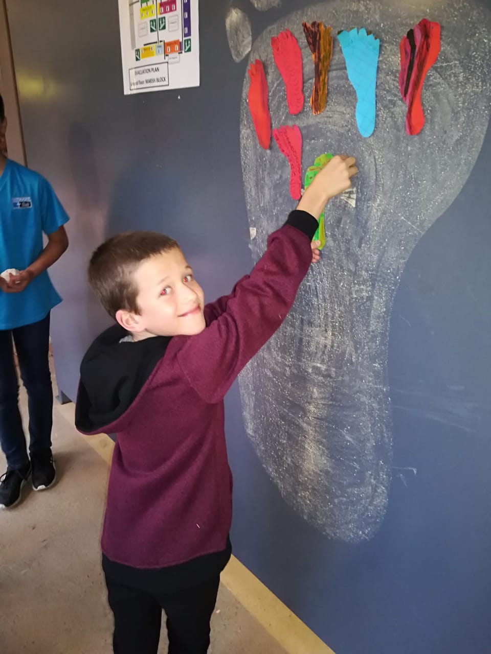 A boy in a purple shirt is drawing a footprint on a wall