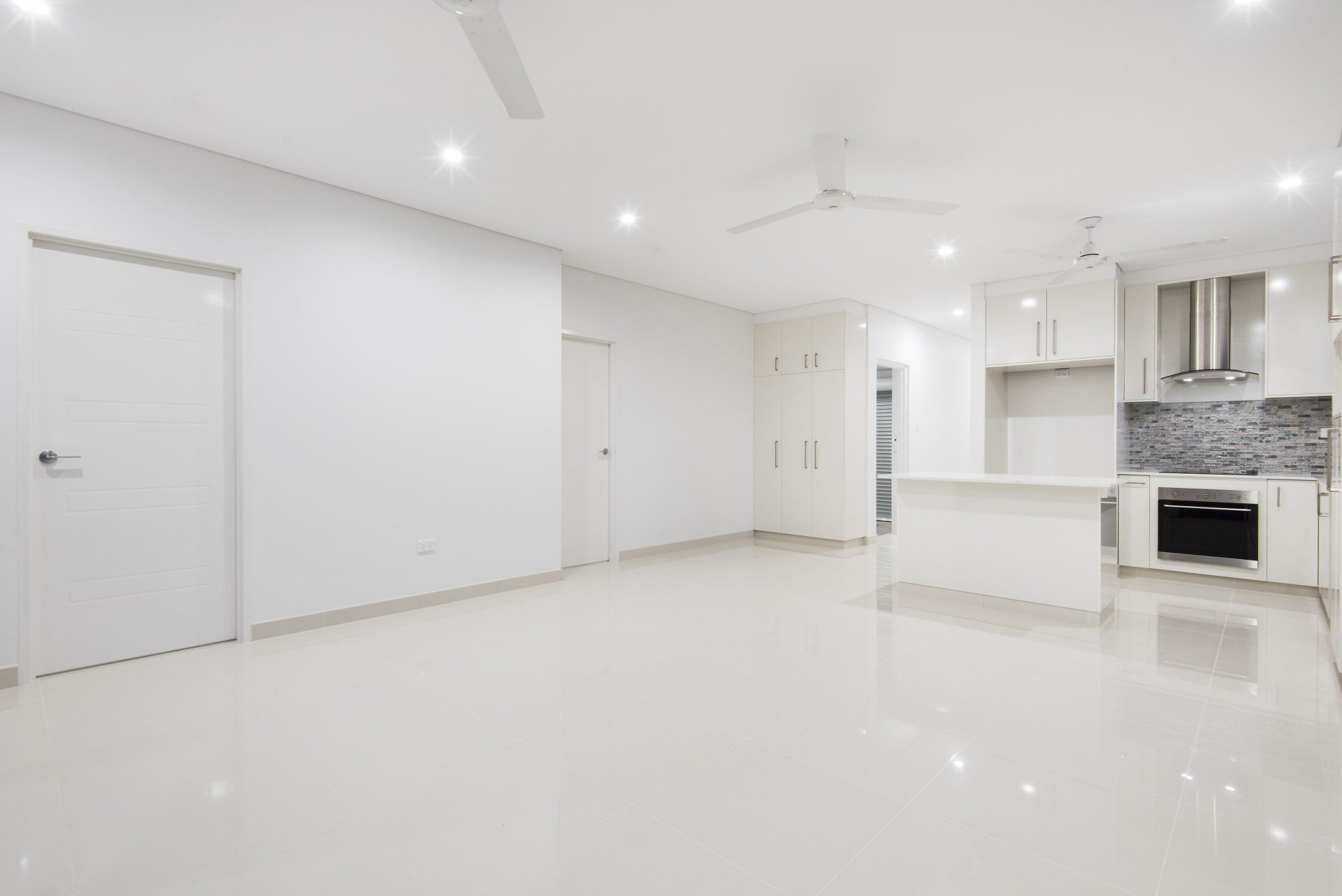 A large empty room with a kitchen and a ceiling fan.