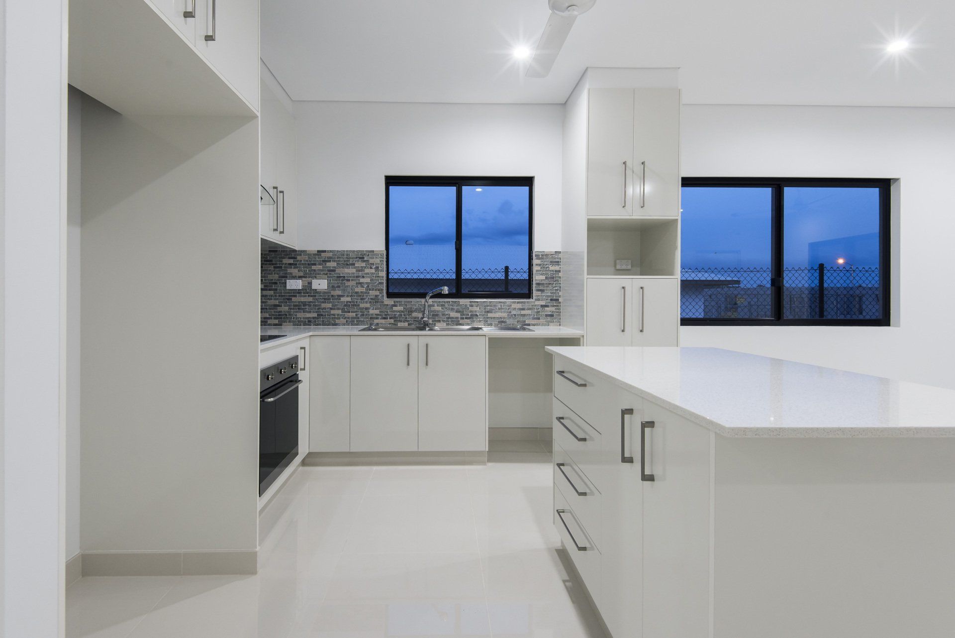 A kitchen with white cabinets , a large island , and two windows.