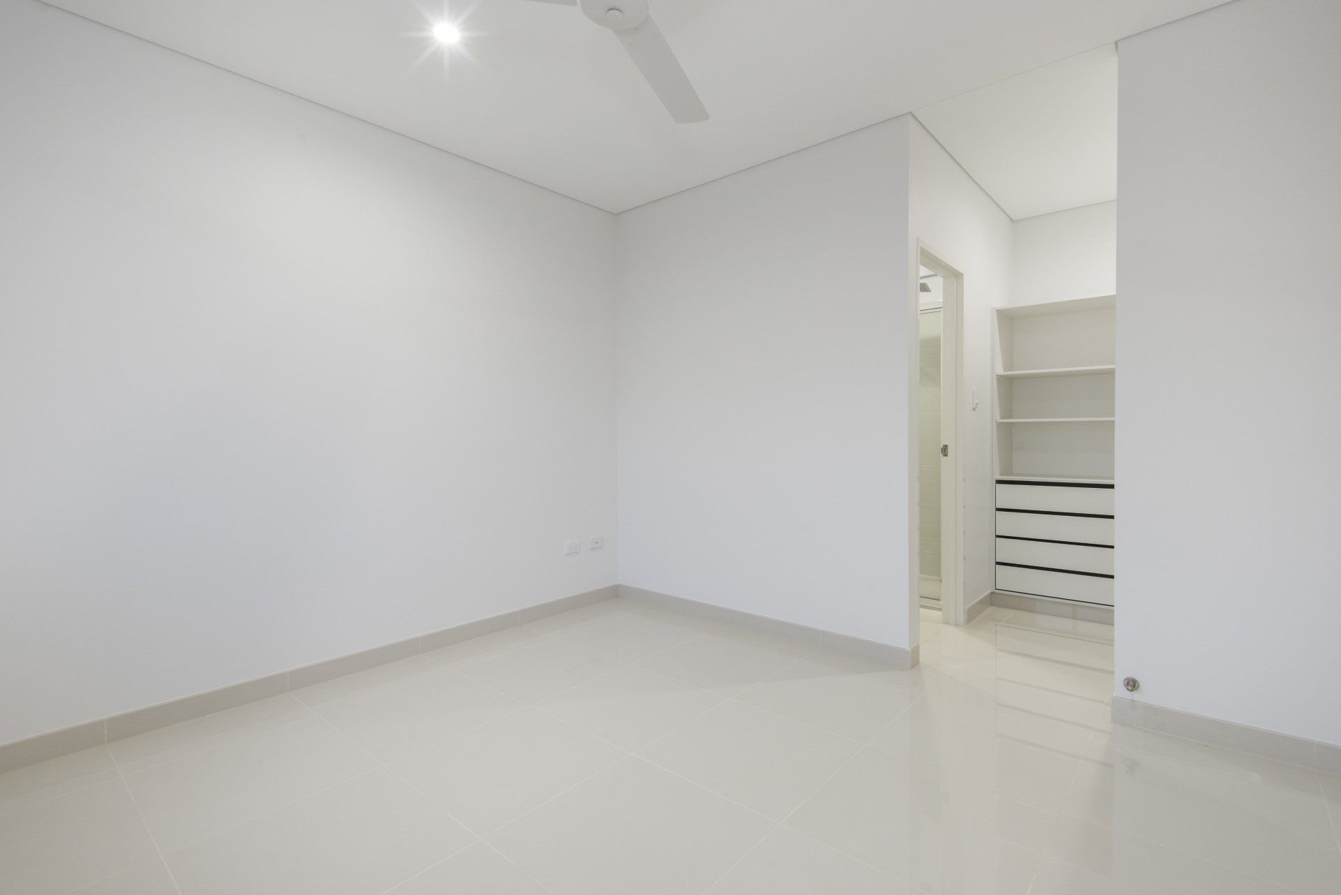 An empty room with white walls and a ceiling fan.