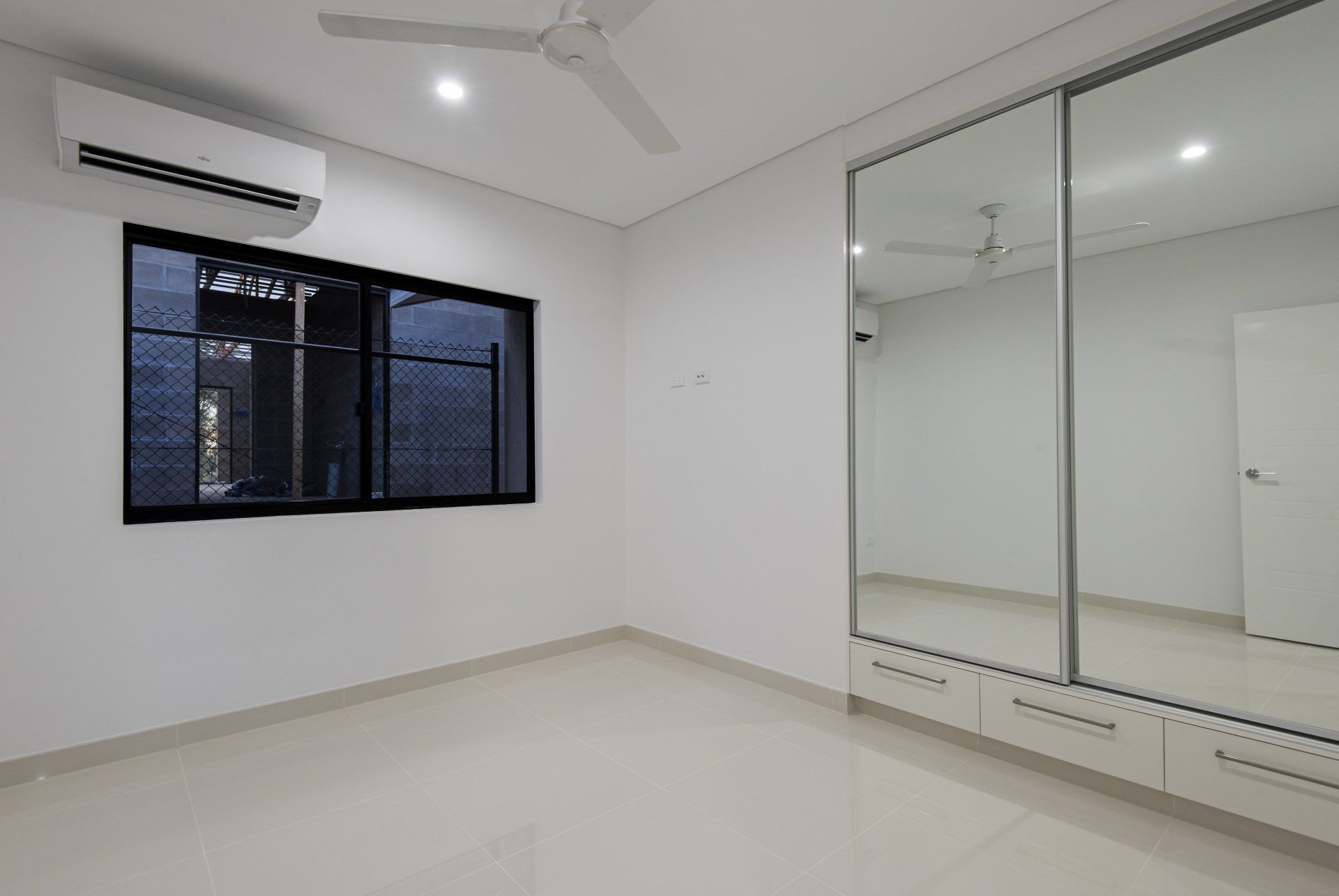 An empty bedroom with a large mirrored wardrobe and a ceiling fan.