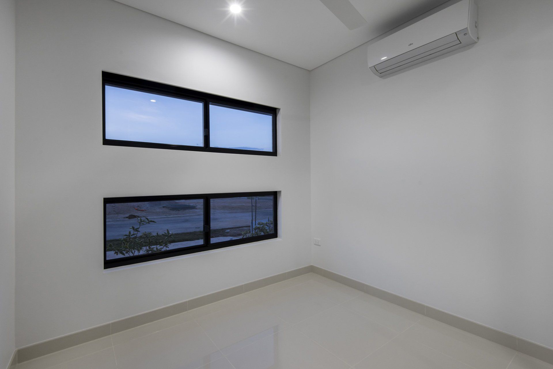 An empty room with two windows and a ceiling fan.