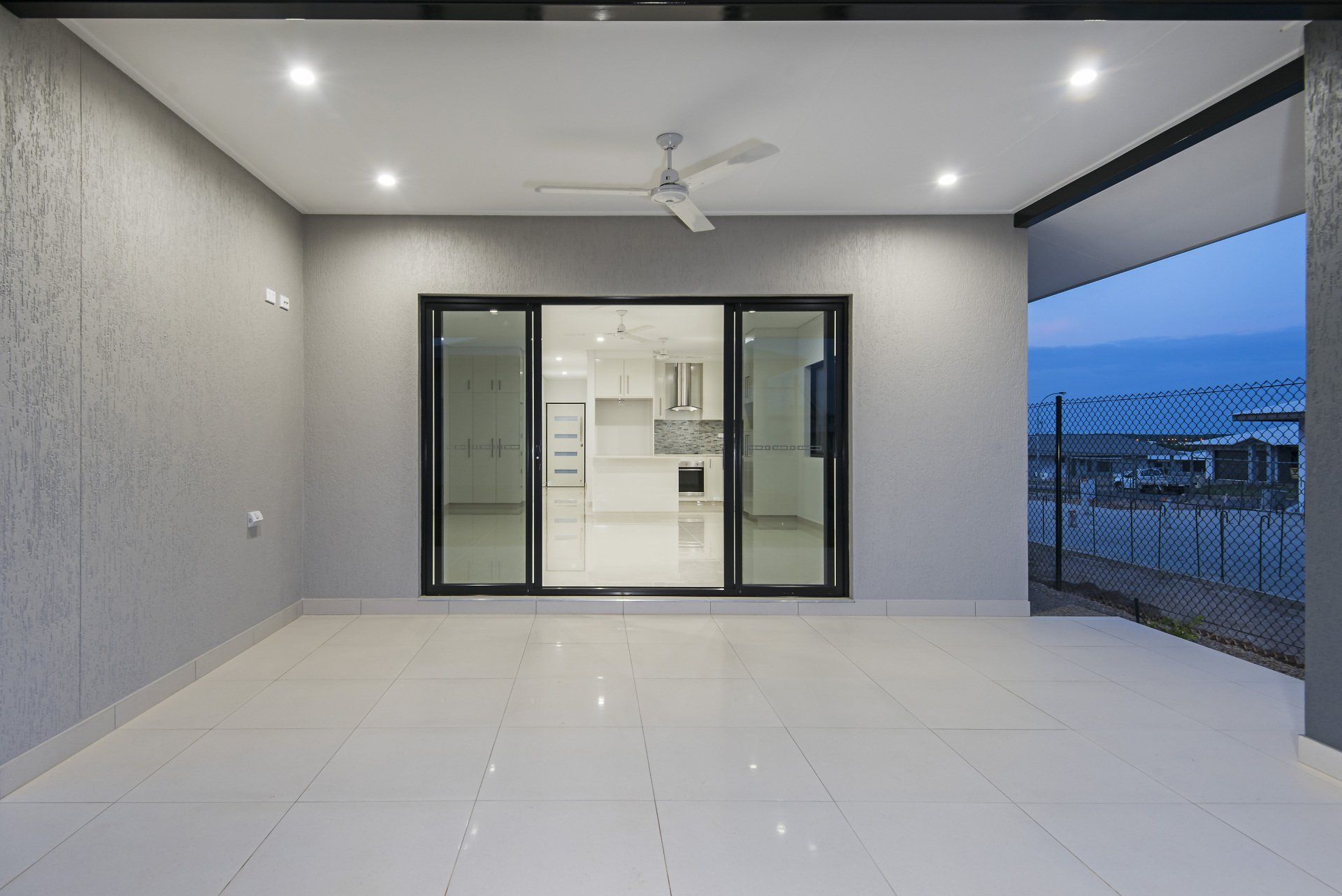 An empty patio with a ceiling fan and sliding glass doors leading to a kitchen.