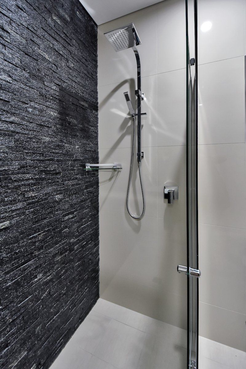 A shower stall with a black brick wall and a glass door