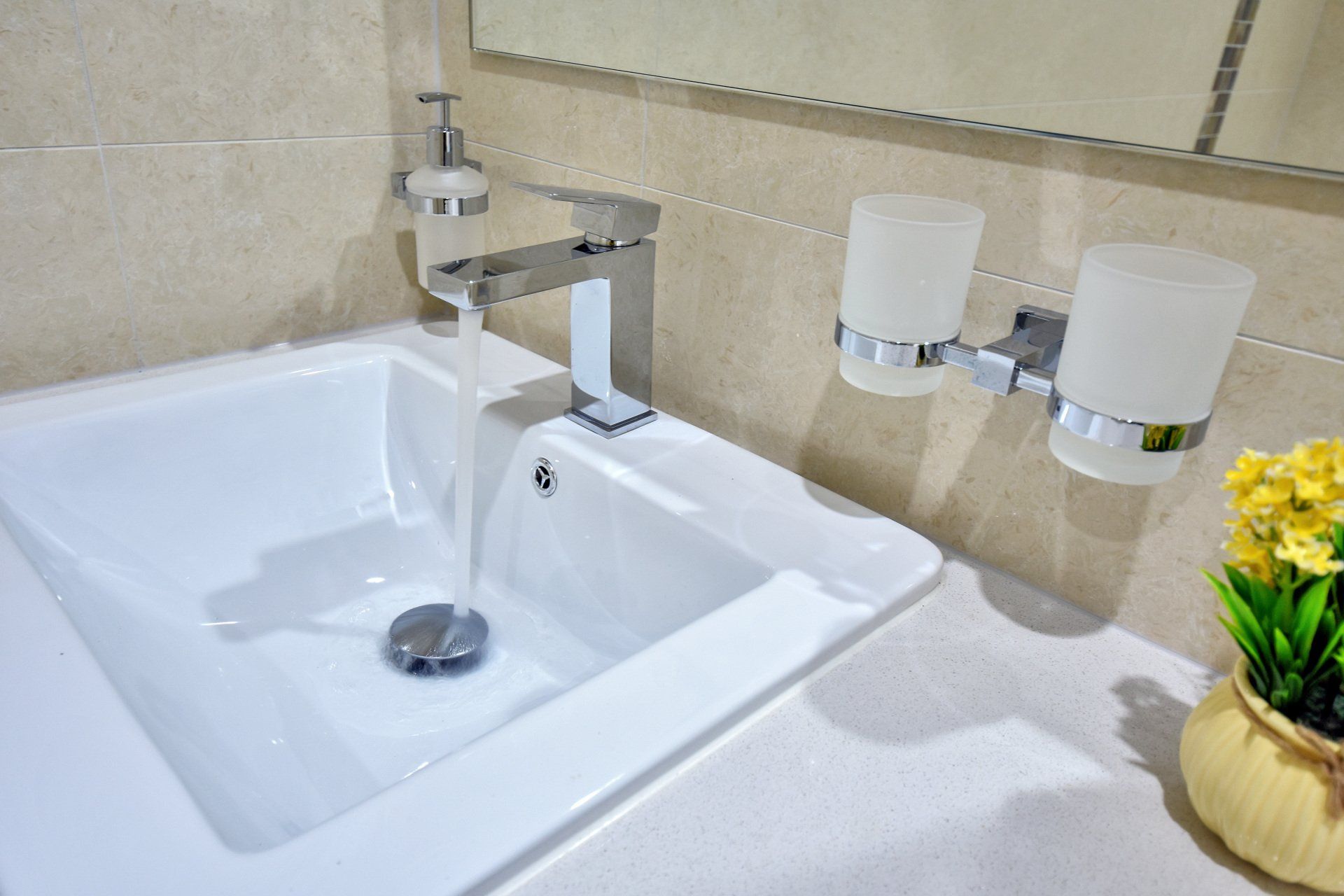 A bathroom sink with water running out of it and a vase of flowers on the counter.