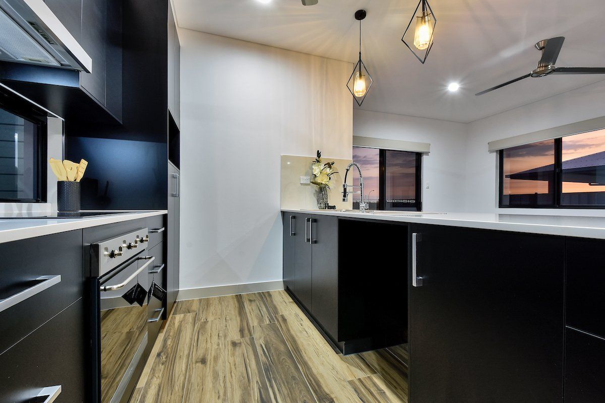 A kitchen with black cabinets , a stove , a sink , and a ceiling fan.