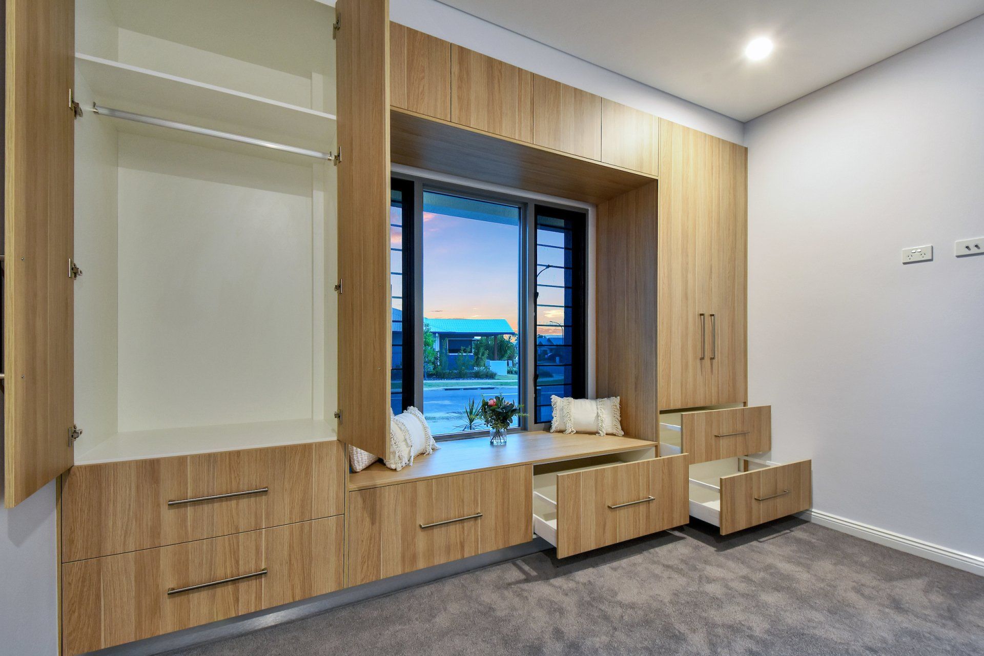 A bedroom with a large window and wooden cabinets.
