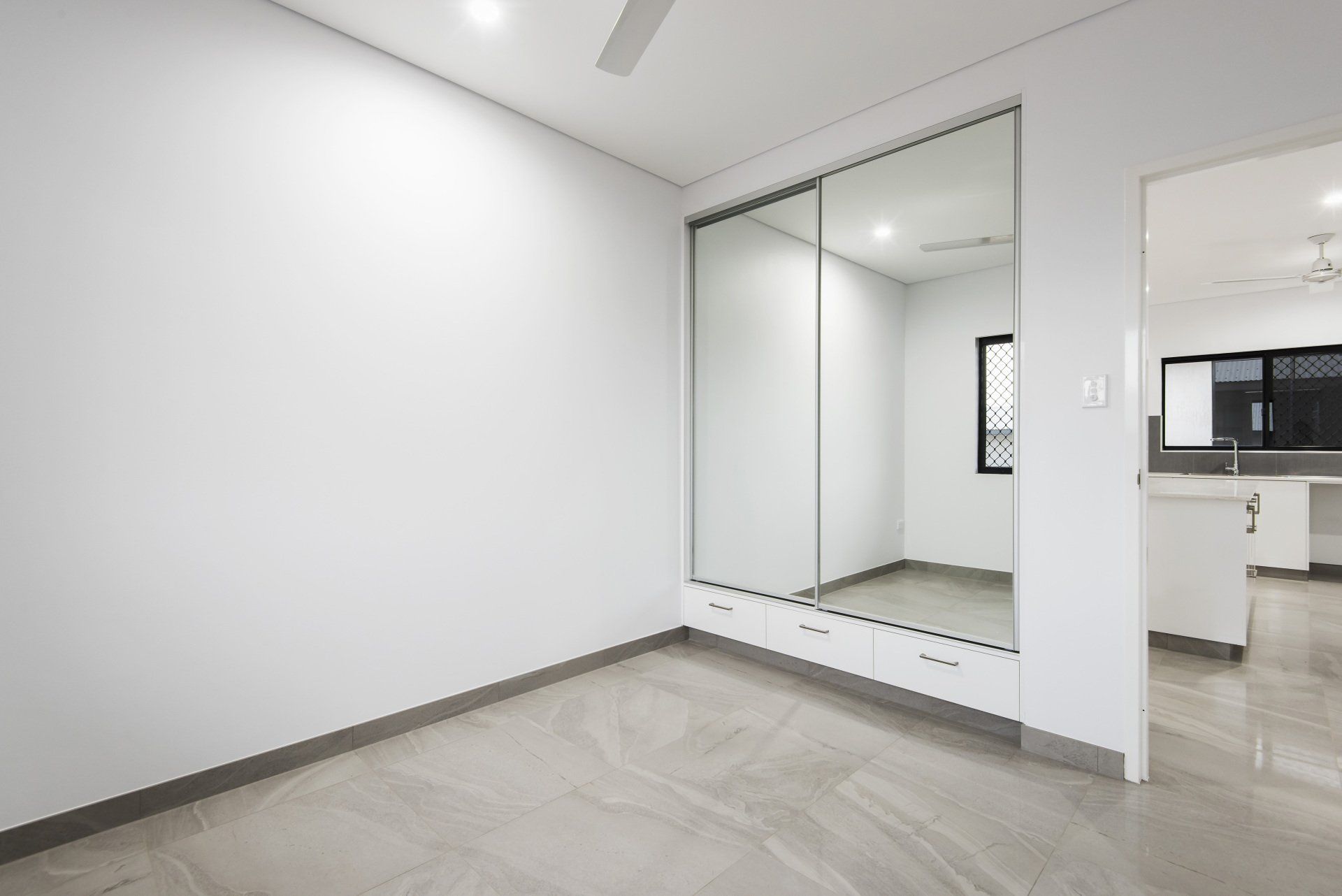 An empty bedroom with a large mirrored wardrobe and a ceiling fan.