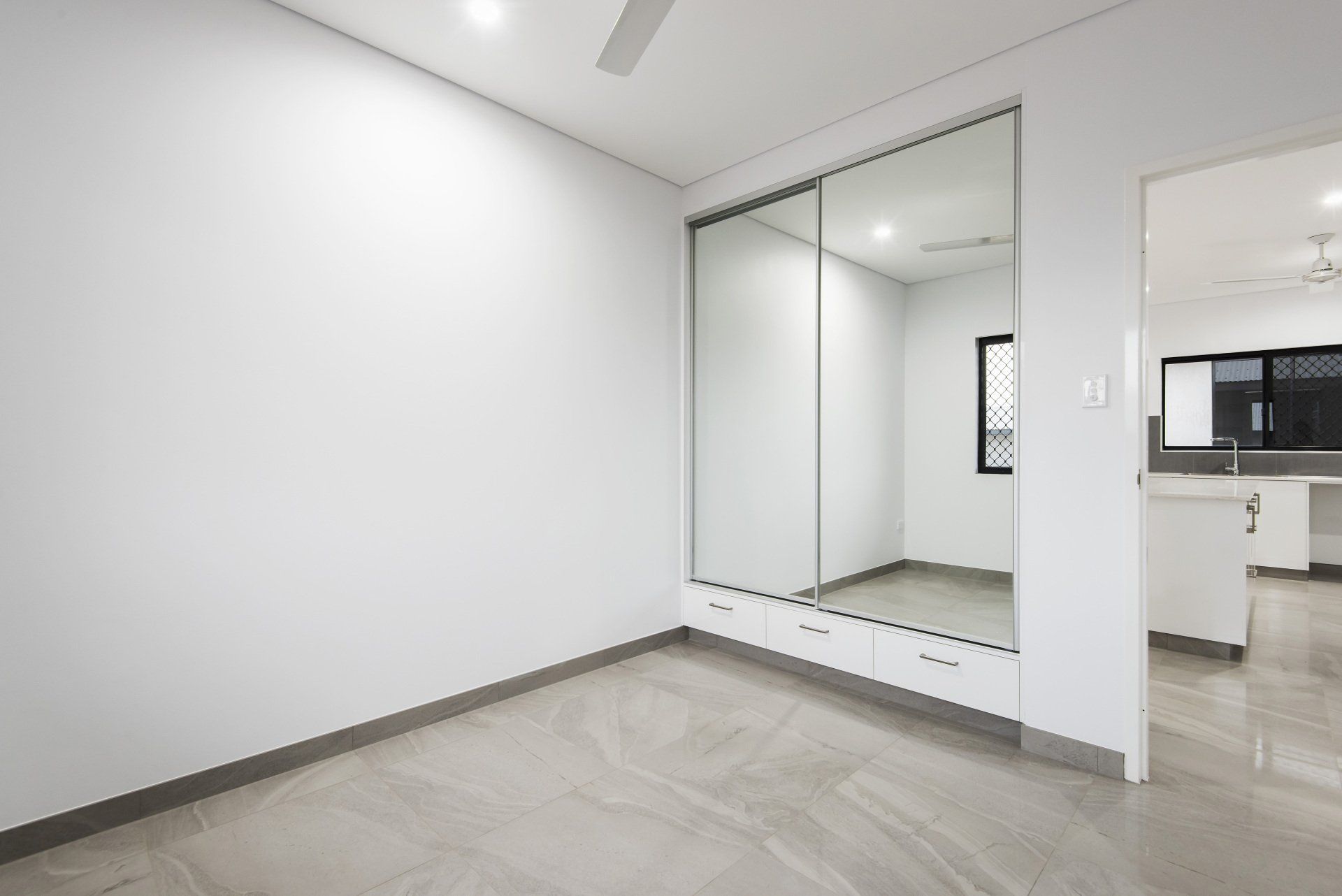 An empty bedroom with a large mirrored wardrobe and a ceiling fan.