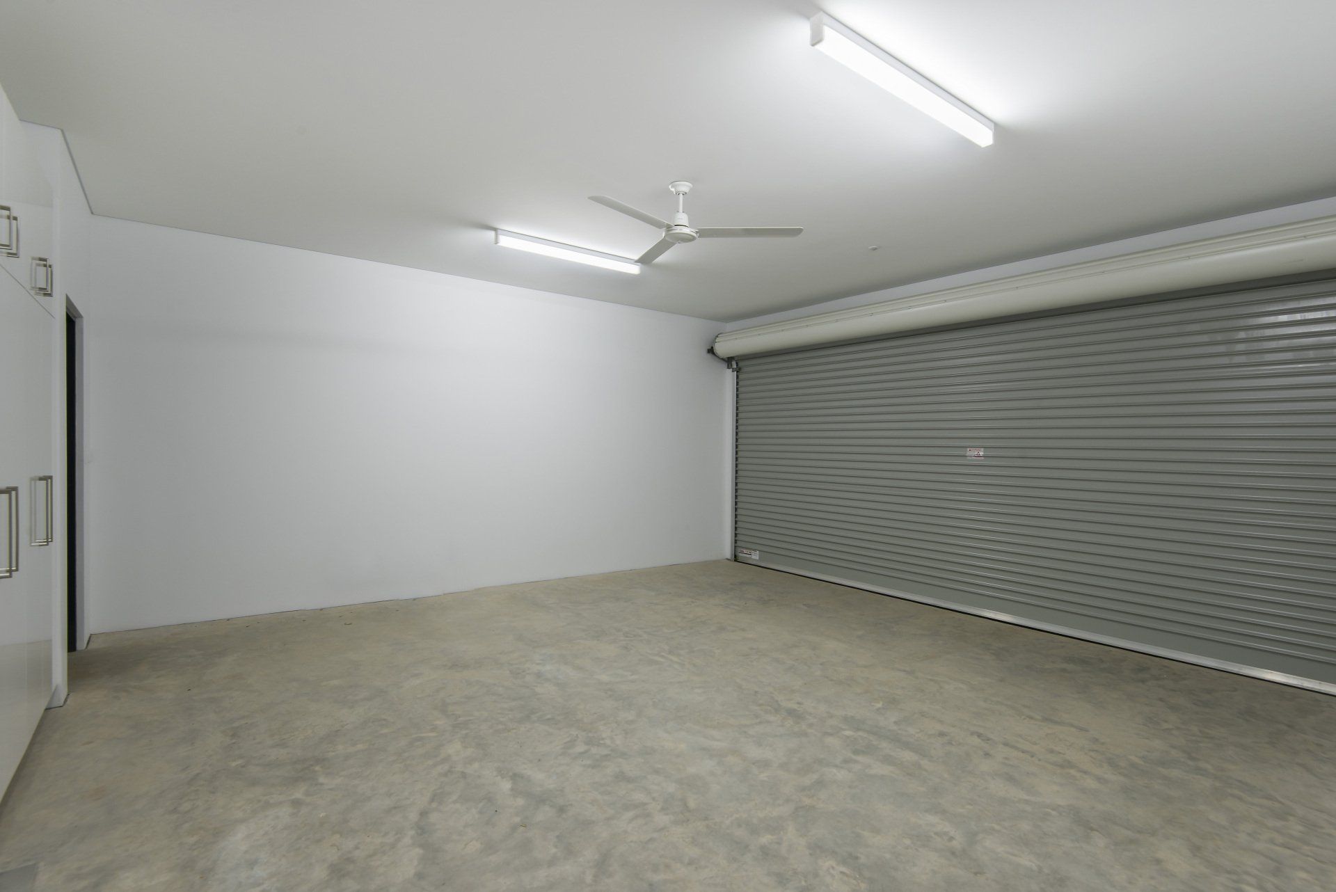 An empty garage with a metal garage door and a ceiling fan.