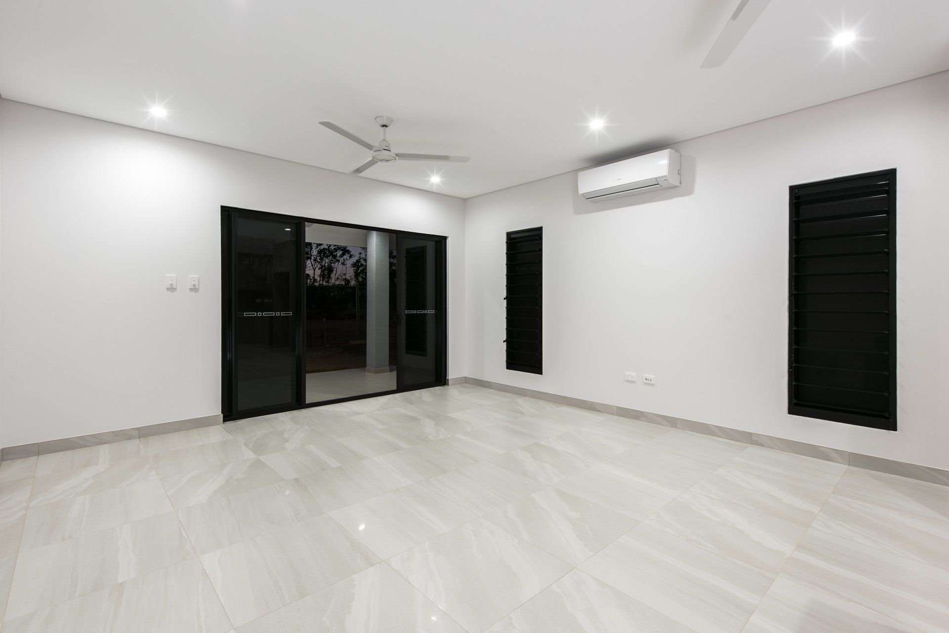 An empty room with a ceiling fan and sliding glass doors.