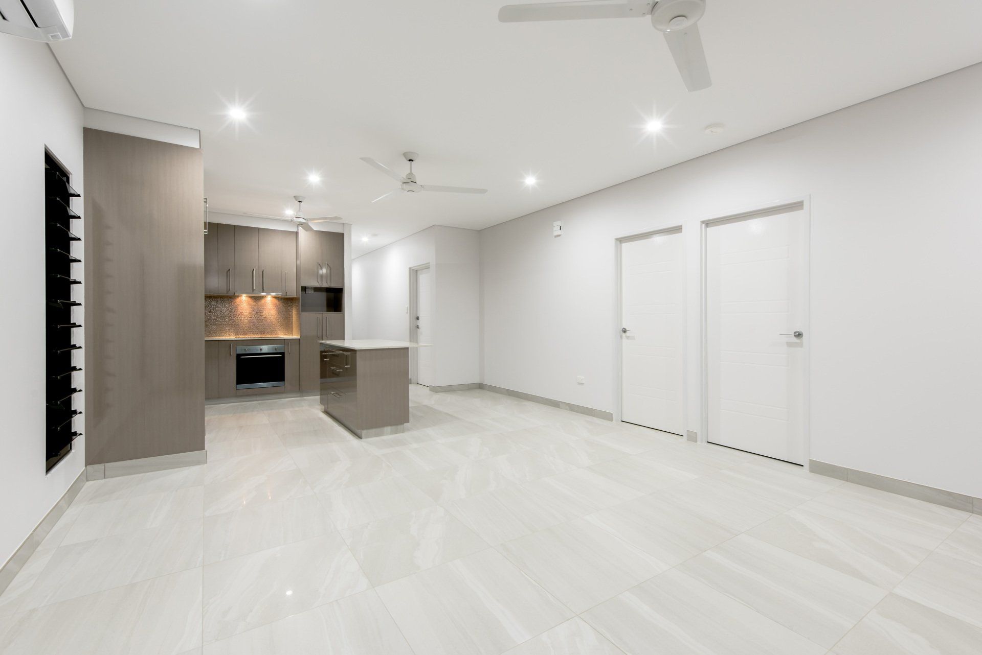 A large empty room with a kitchen and a ceiling fan.