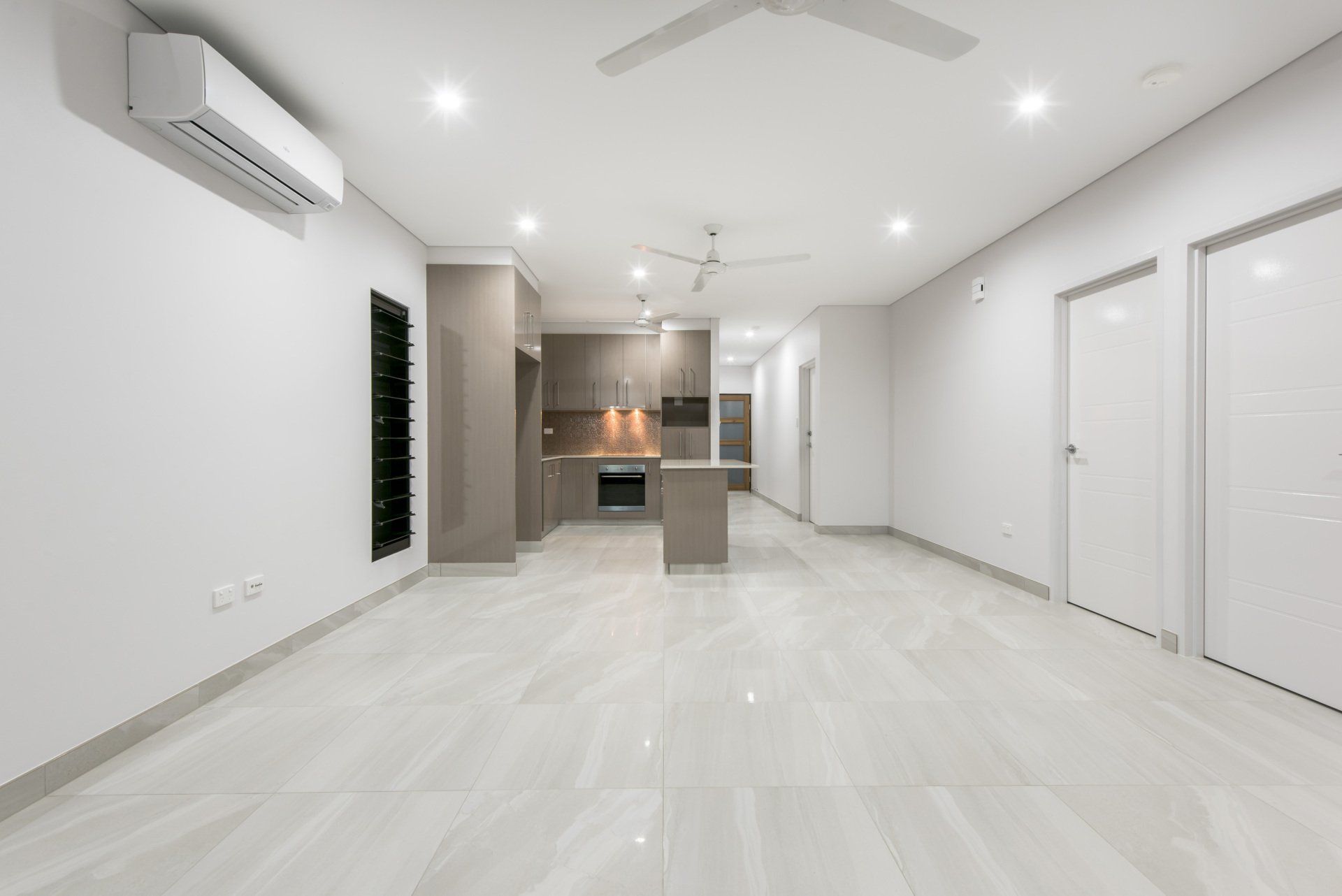 A large empty room with a kitchen and a ceiling fan.