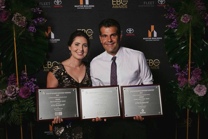 A man and a woman are standing next to each other holding three plaques.