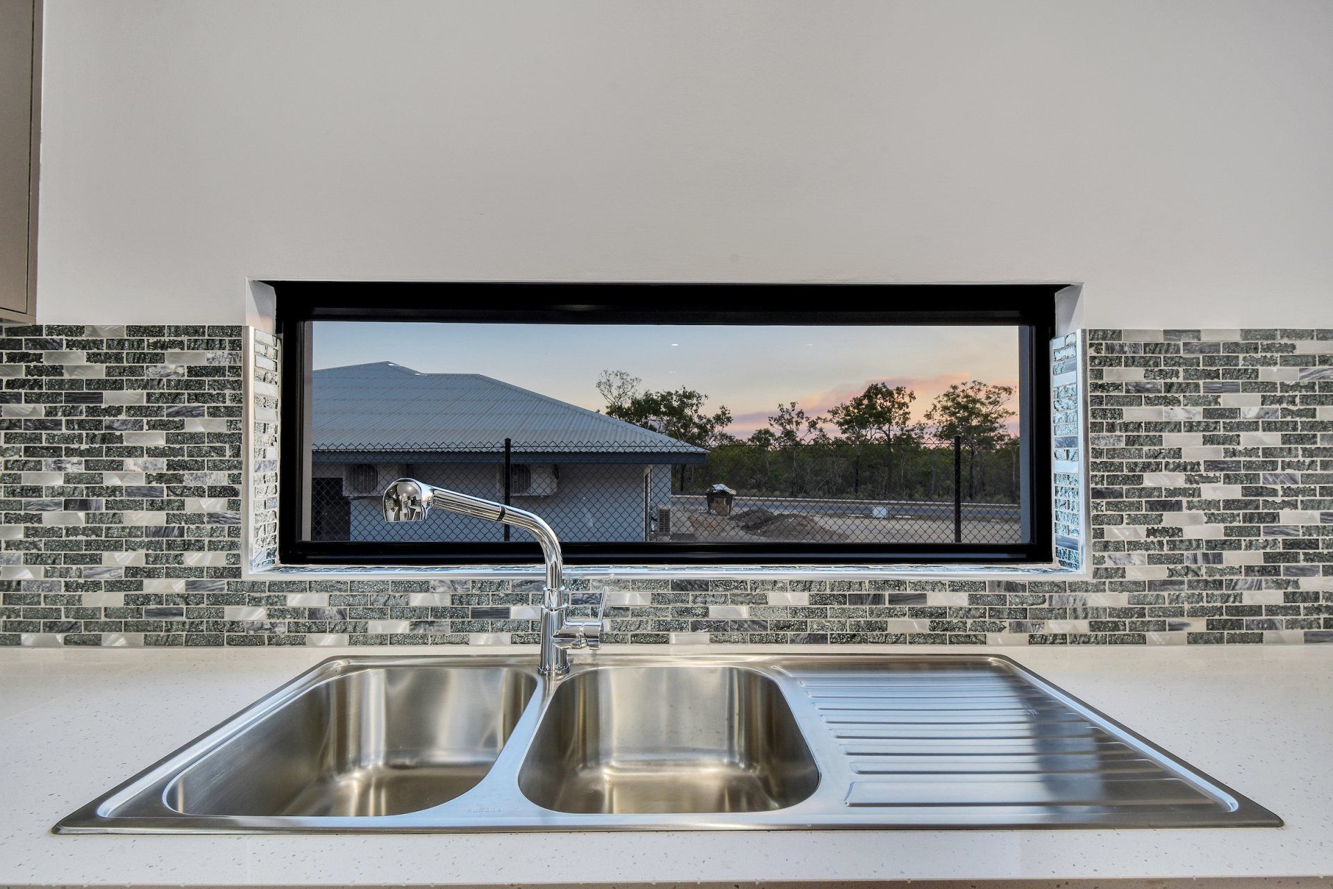A kitchen sink with a view of a house through a window.