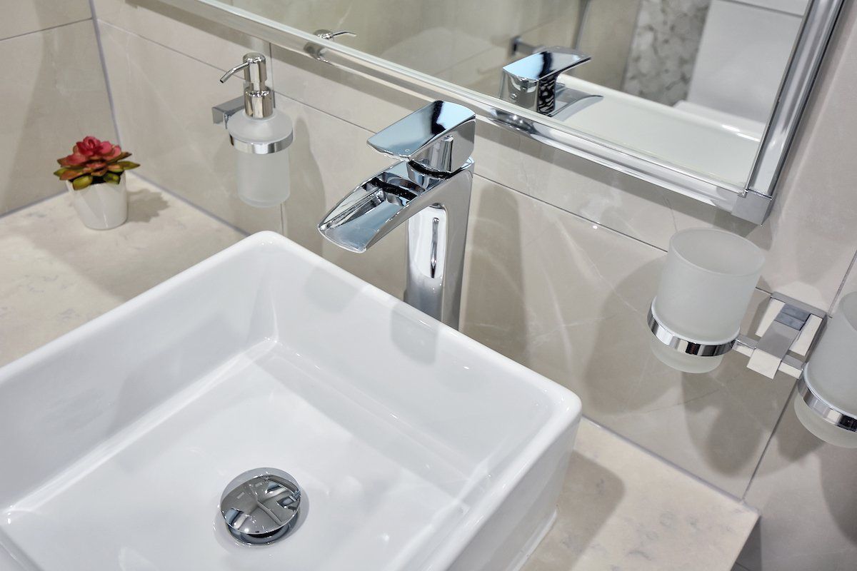 A bathroom with a sink , mirror and soap dispenser.