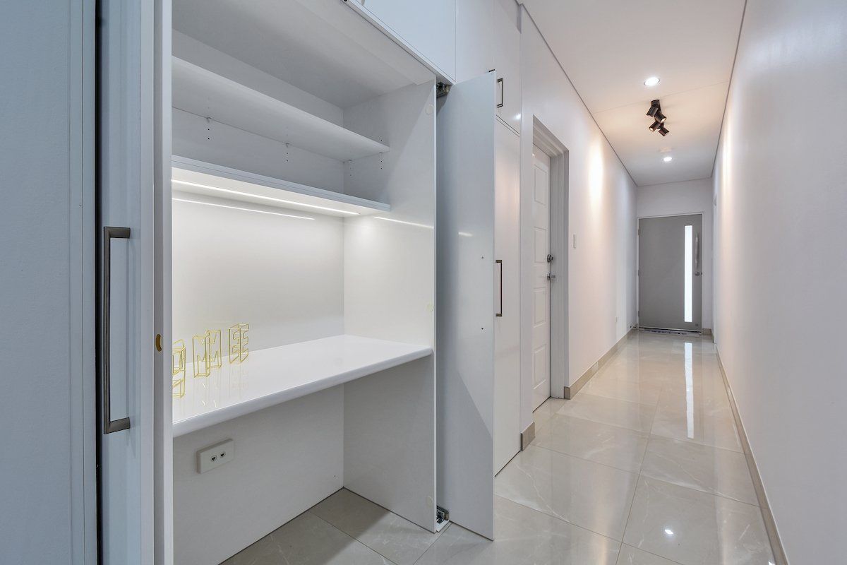 A hallway with a desk and shelves in the corner.