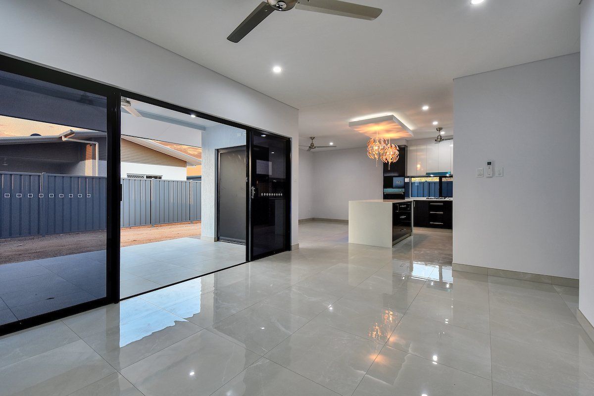 An empty living room with a ceiling fan and sliding glass doors leading to a kitchen.