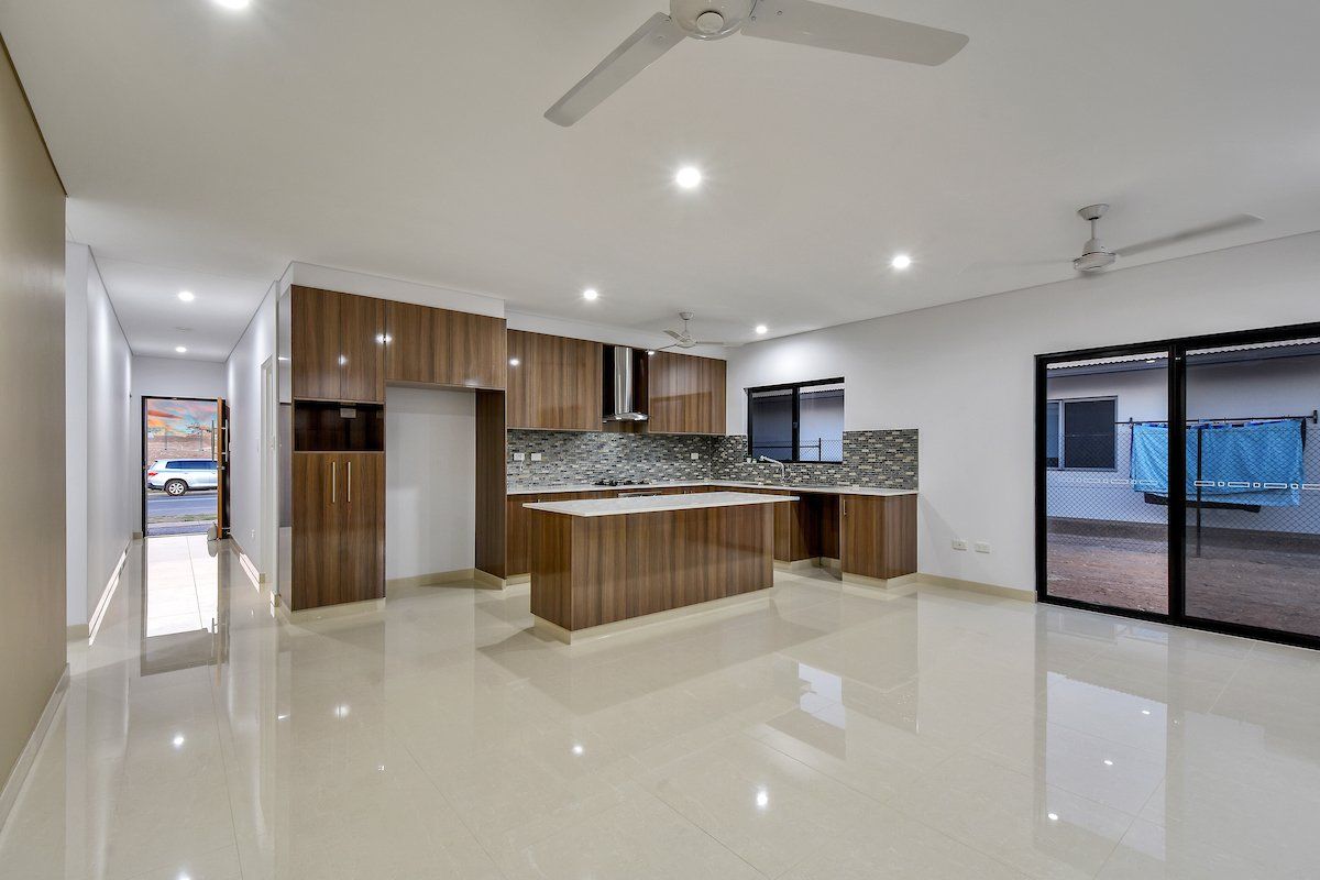 A large empty room with a kitchen and a ceiling fan.