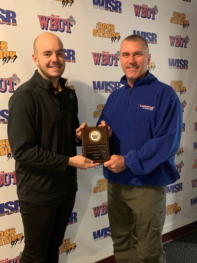 Two men holding an award, smiling, in front of a logo wall.