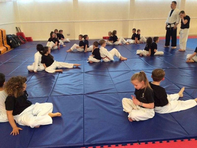A group of kids are sitting on a mat in a gym