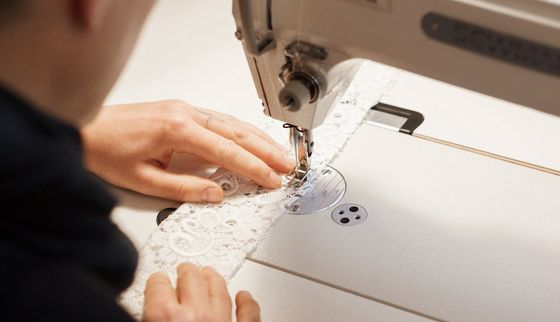 Nahaufnahme von einer Person, die an einer Naehmaschine ein Kleidungsstück für eine Braut zusammennaeht