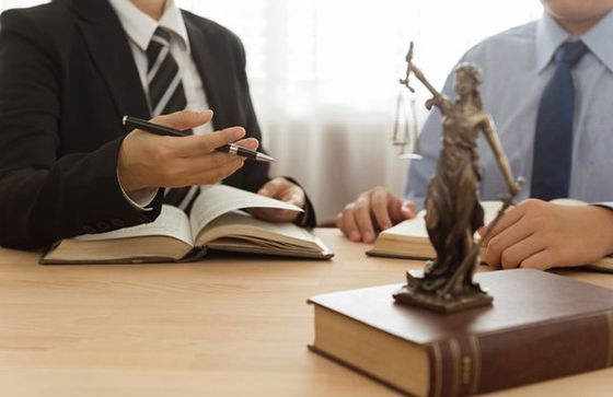 Two lawyers are sitting at a table with a statue of justice.