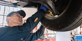 A mechanic in a black uniform and hat working on a car tire, in a shop.