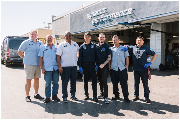 Group of men in work uniforms stand outside a business with