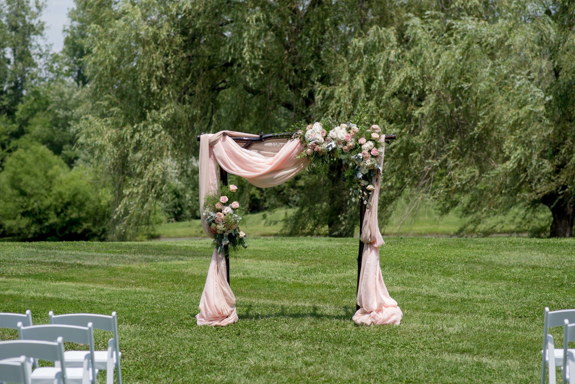Pink floral wedding arch on a green lawn with trees in the background
