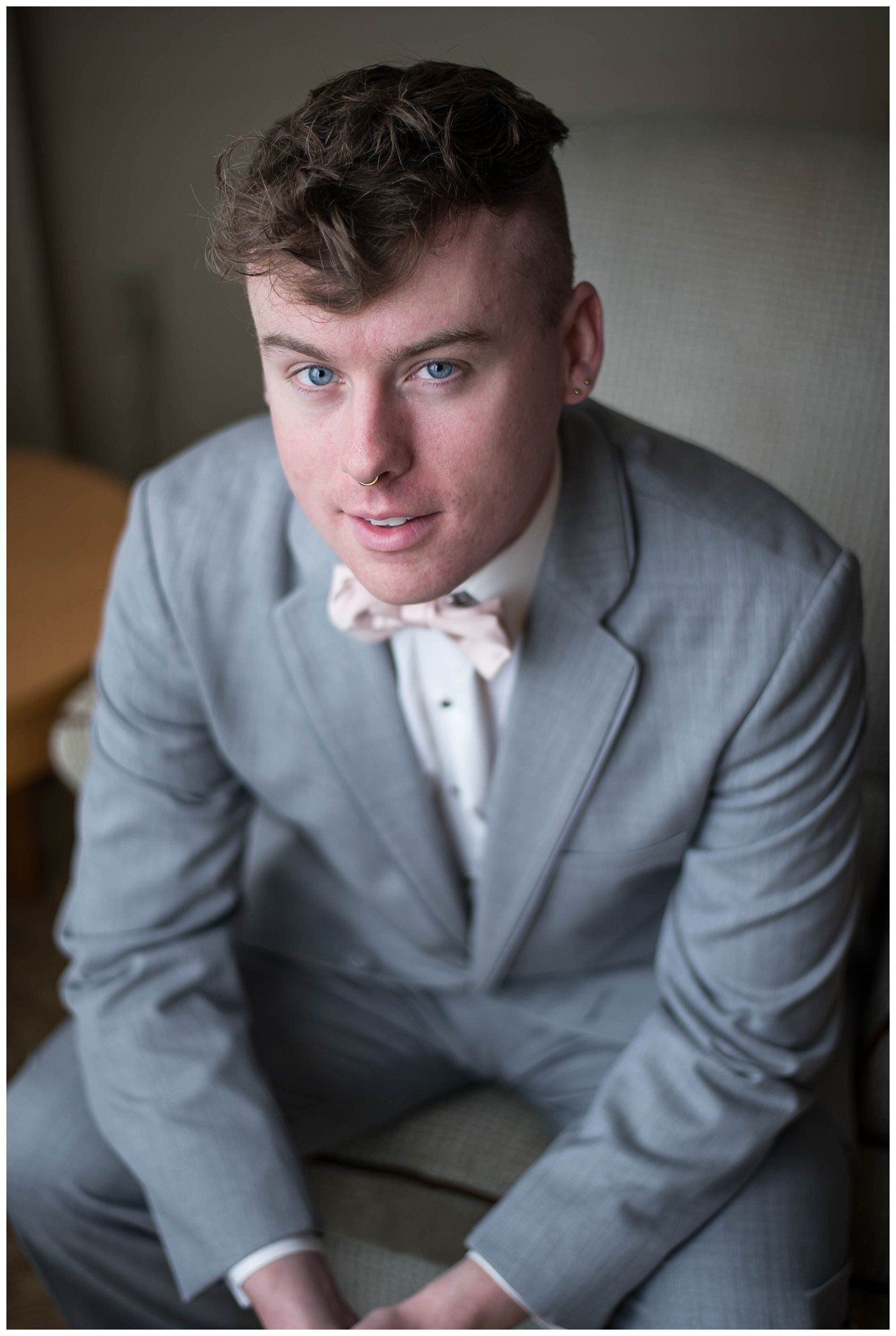 Man in a light gray suit and pink bow tie, seated indoors and looking at the camera.