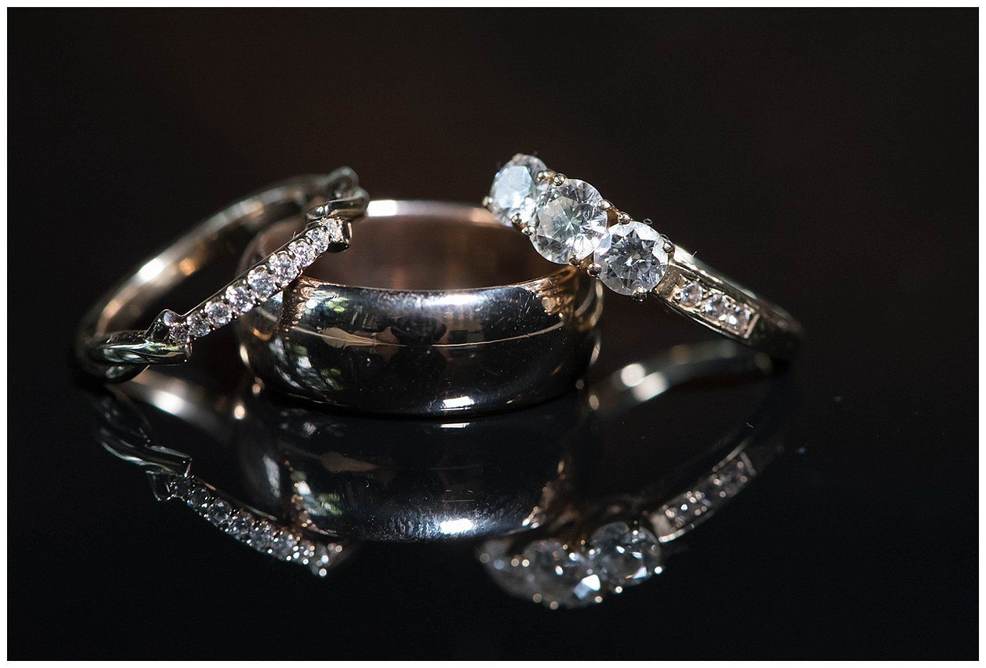 Wedding rings with diamonds on a glossy black surface, reflected below.