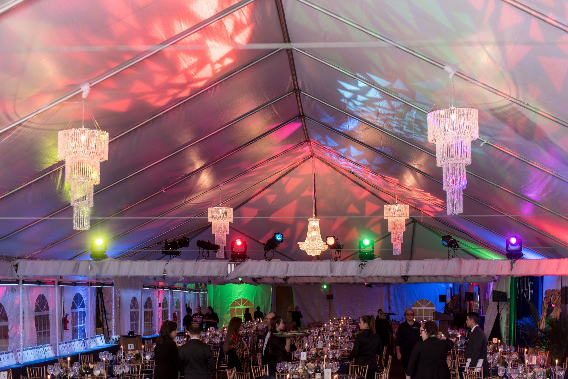 Lit tent venue with colorful chandeliers and guests seated at tables for an event