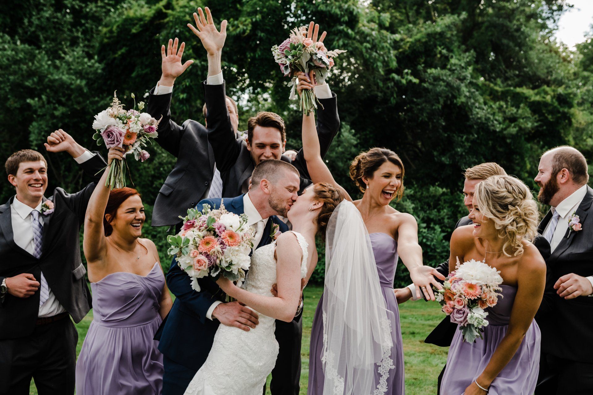 Wedding party celebrates outdoors, raising bouquets and cheering in a garden