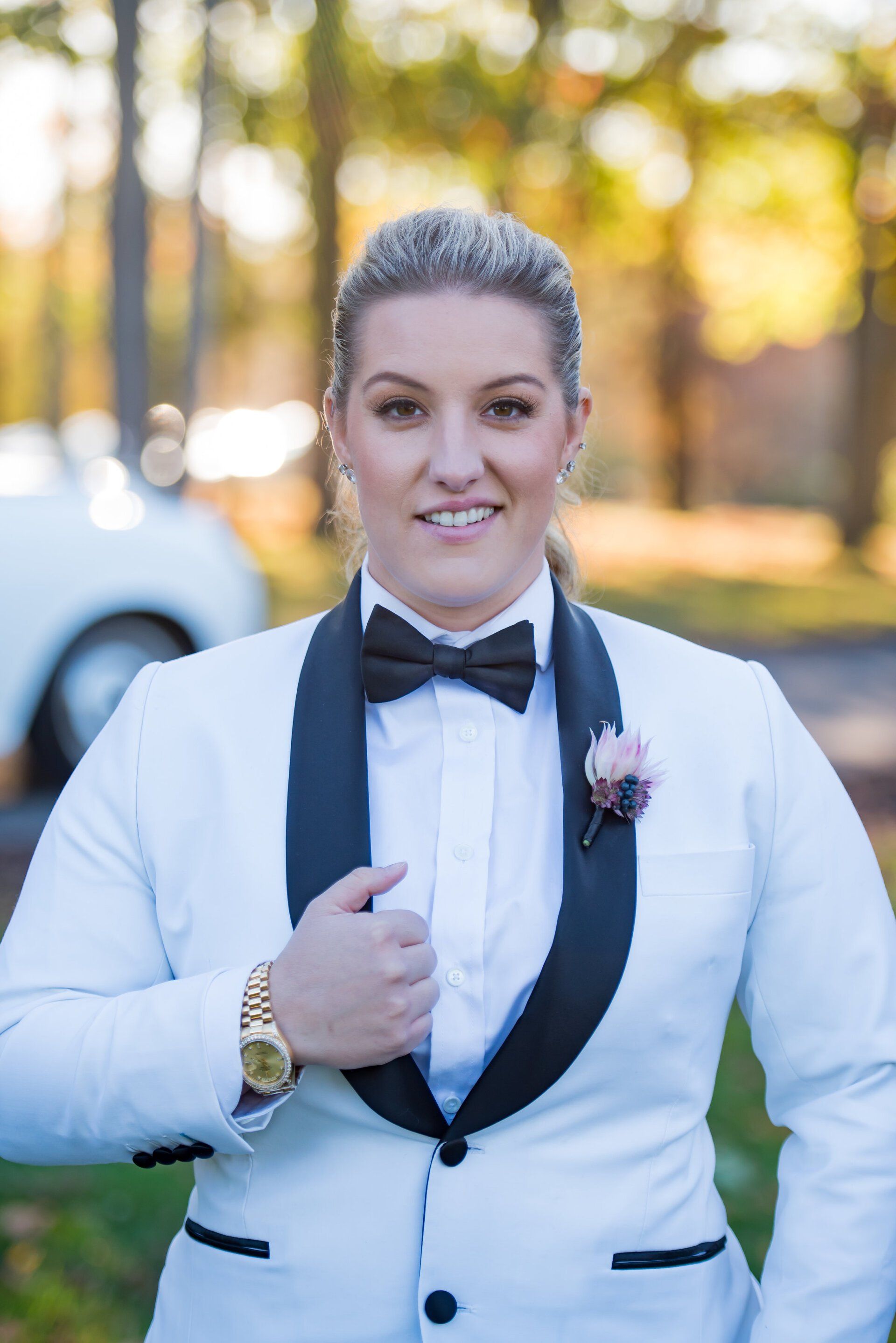 Person in a white tuxedo jacket with black lapels, standing outdoors and adjusting their jacket.