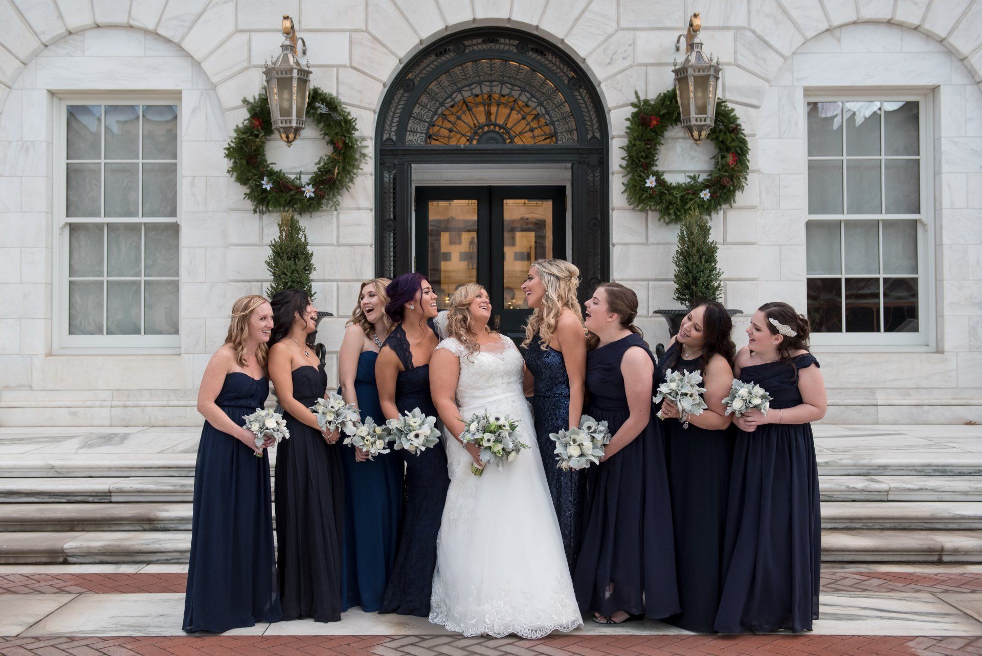 Bride and bridesmaids in navy dresses posing on church steps with white floral bouquets