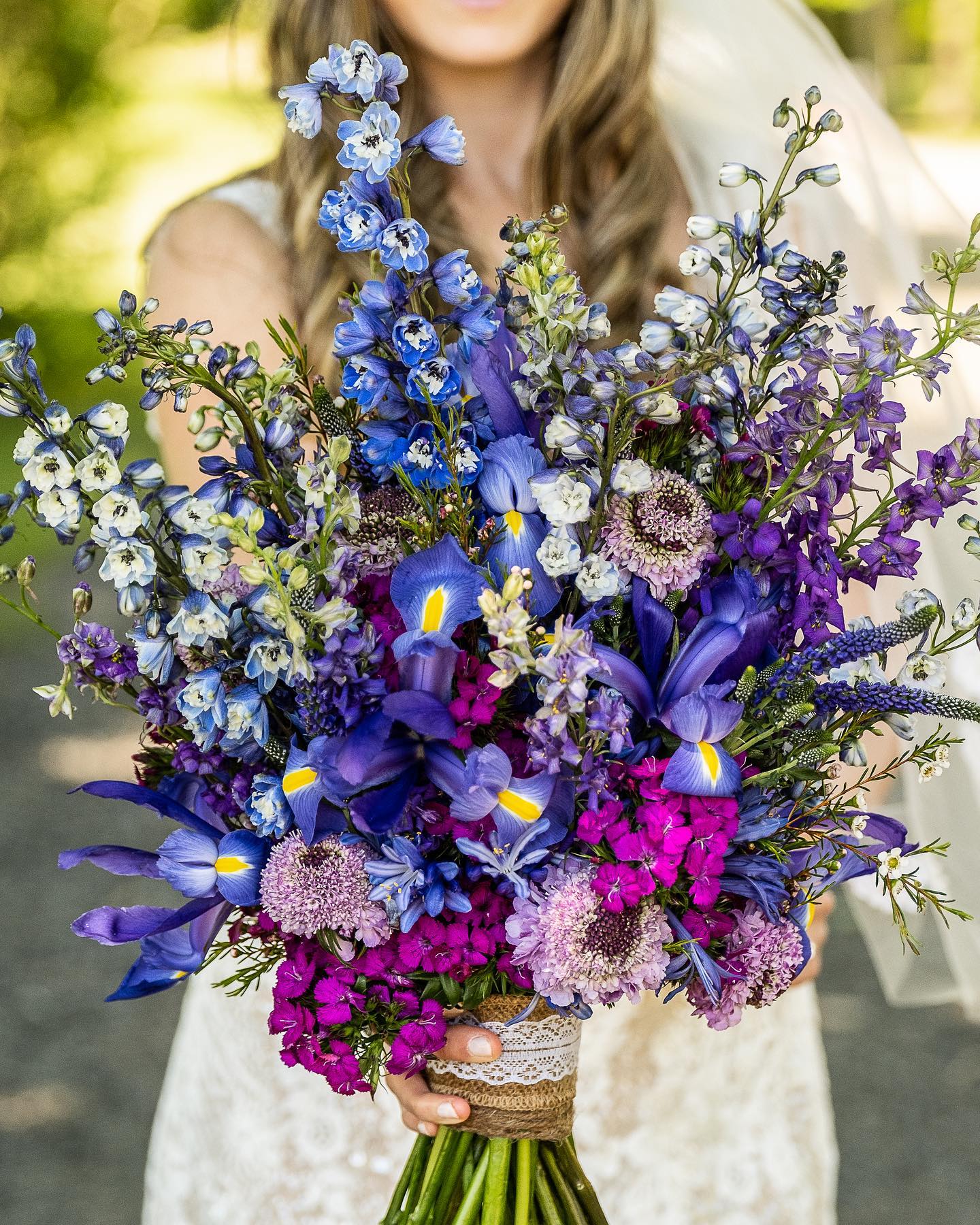 Bouquet of blue, purple, and magenta flowers held by a person in a white dress