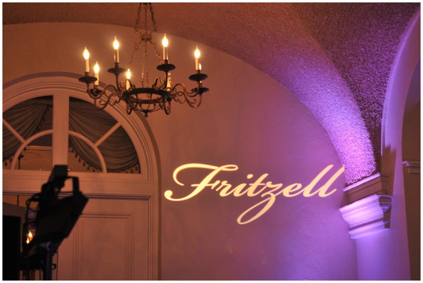 Gold “Fritzell” sign on a pink-lit wall beside a chandelier and arched doorway