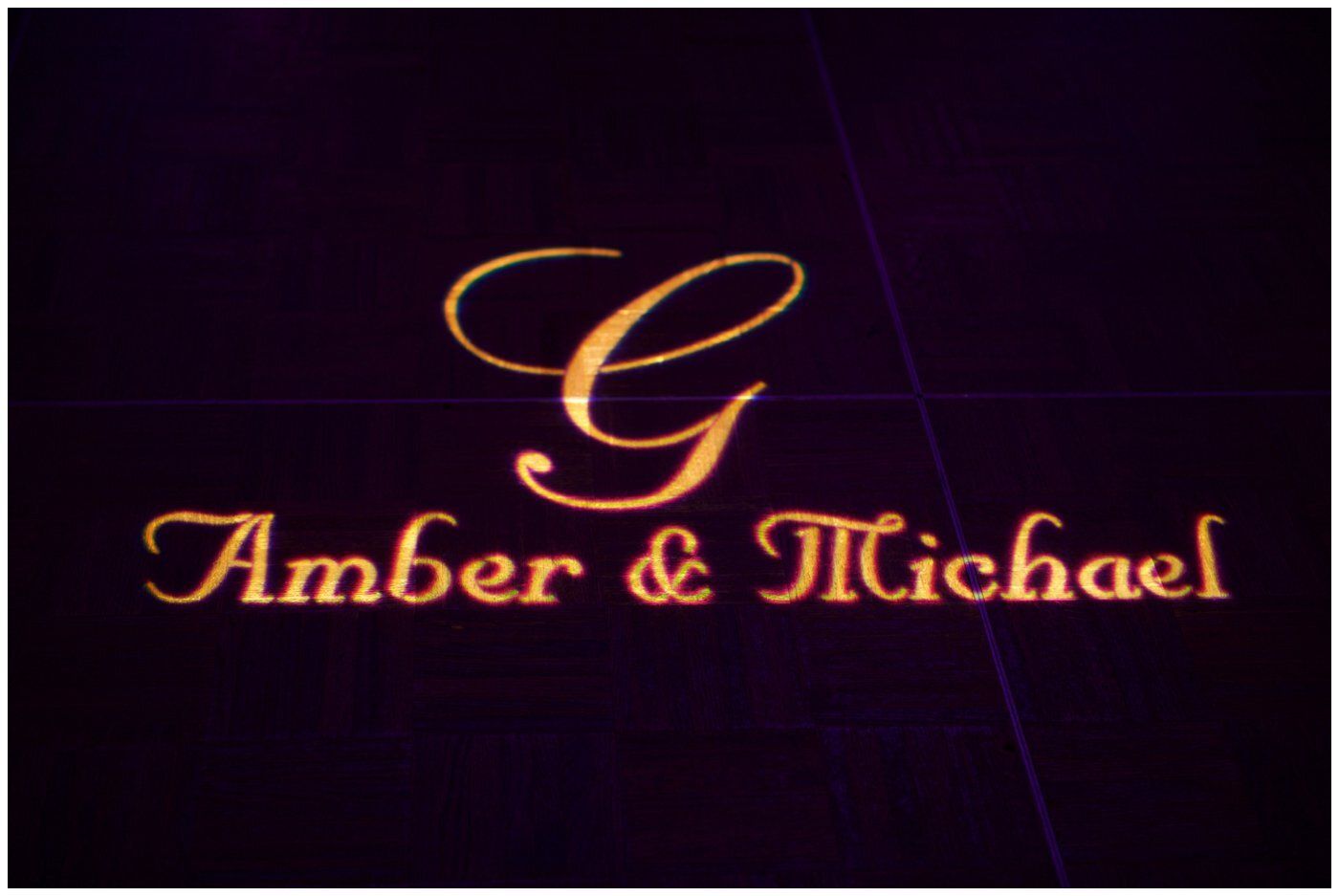Gold script monogram “G” above “Amber & Michael” on a dark purple background.