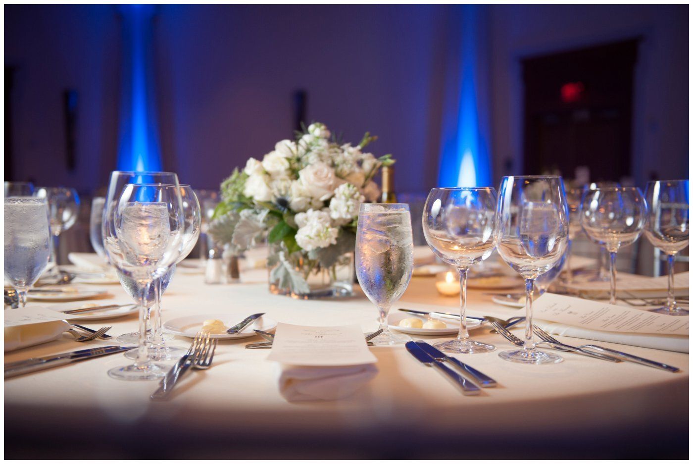 Elegant banquet table with white floral centerpiece, wine glasses, and blue uplighting in the background