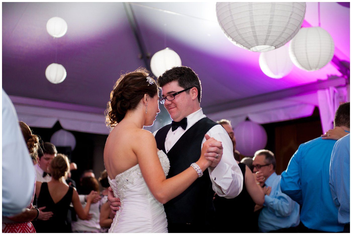 Couple slow dancing at a wedding reception under purple lighting and hanging lanterns