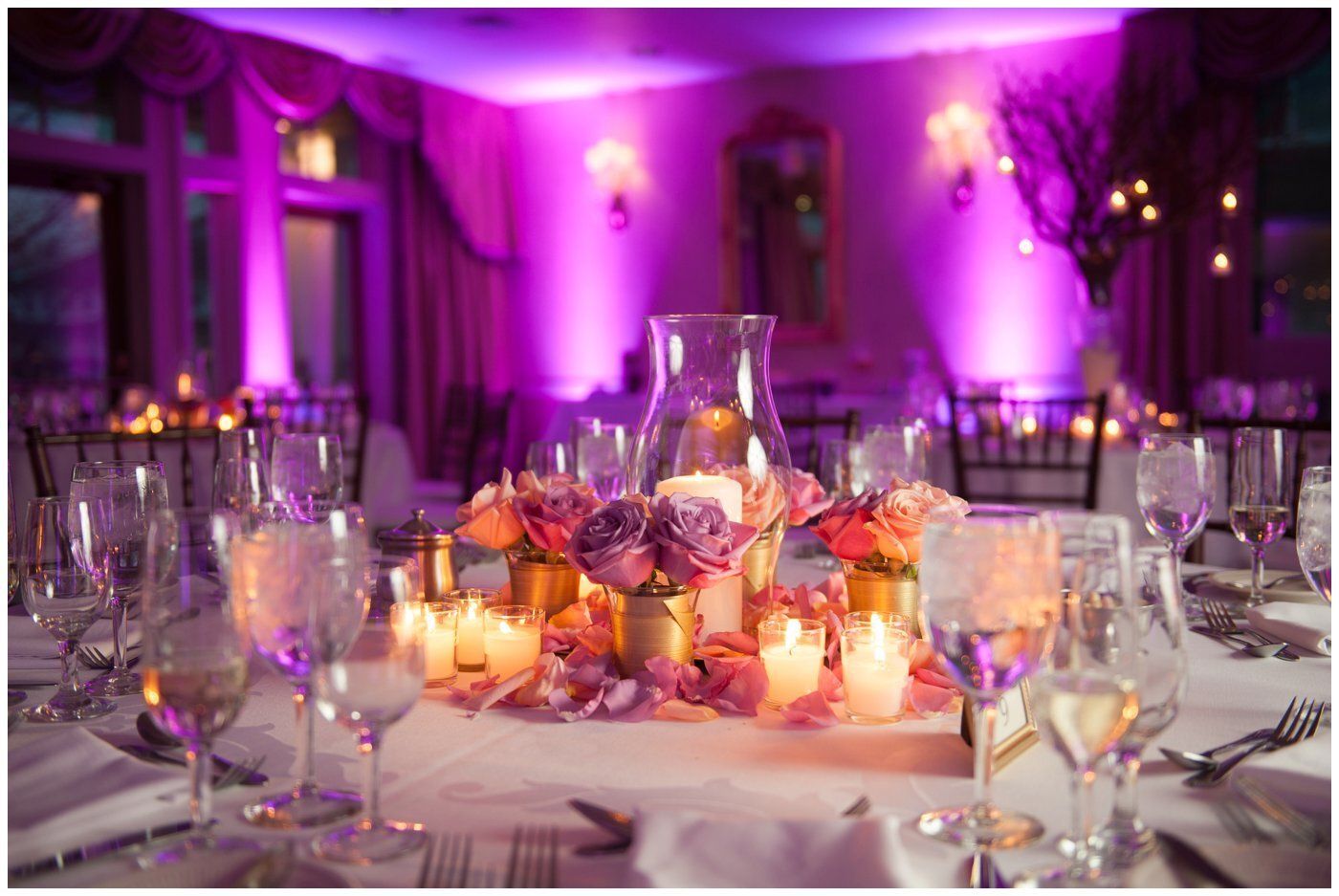 Purple-lit banquet table with candles, flowers, and glassware in an elegant event hall