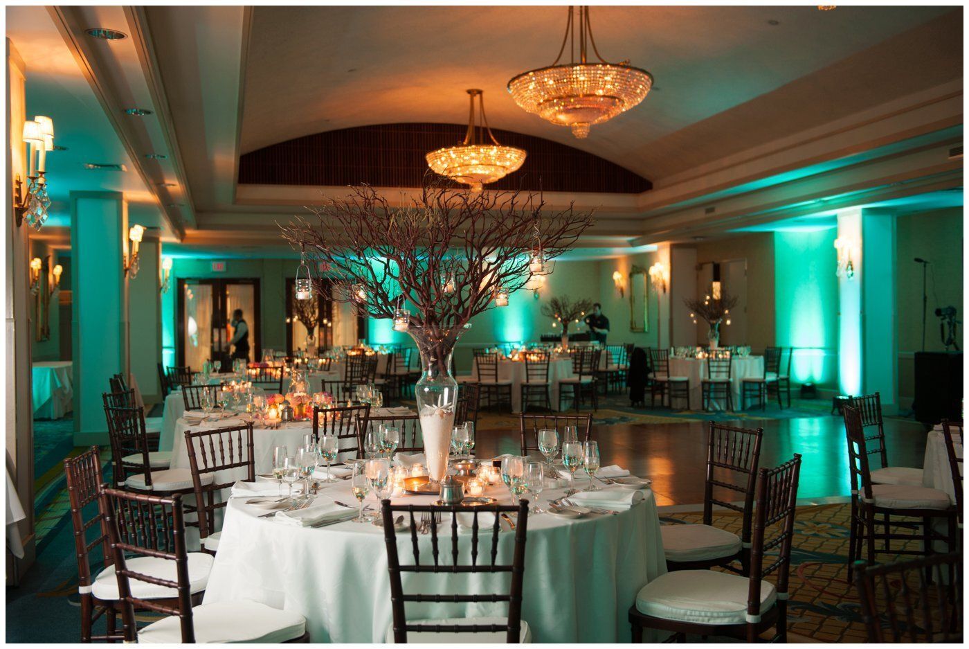 Elegant banquet hall with round tables, white tablecloths, and teal accent lighting