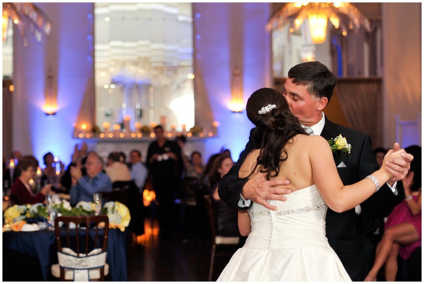Couple dancing at a candlelit wedding reception with guests in the background
