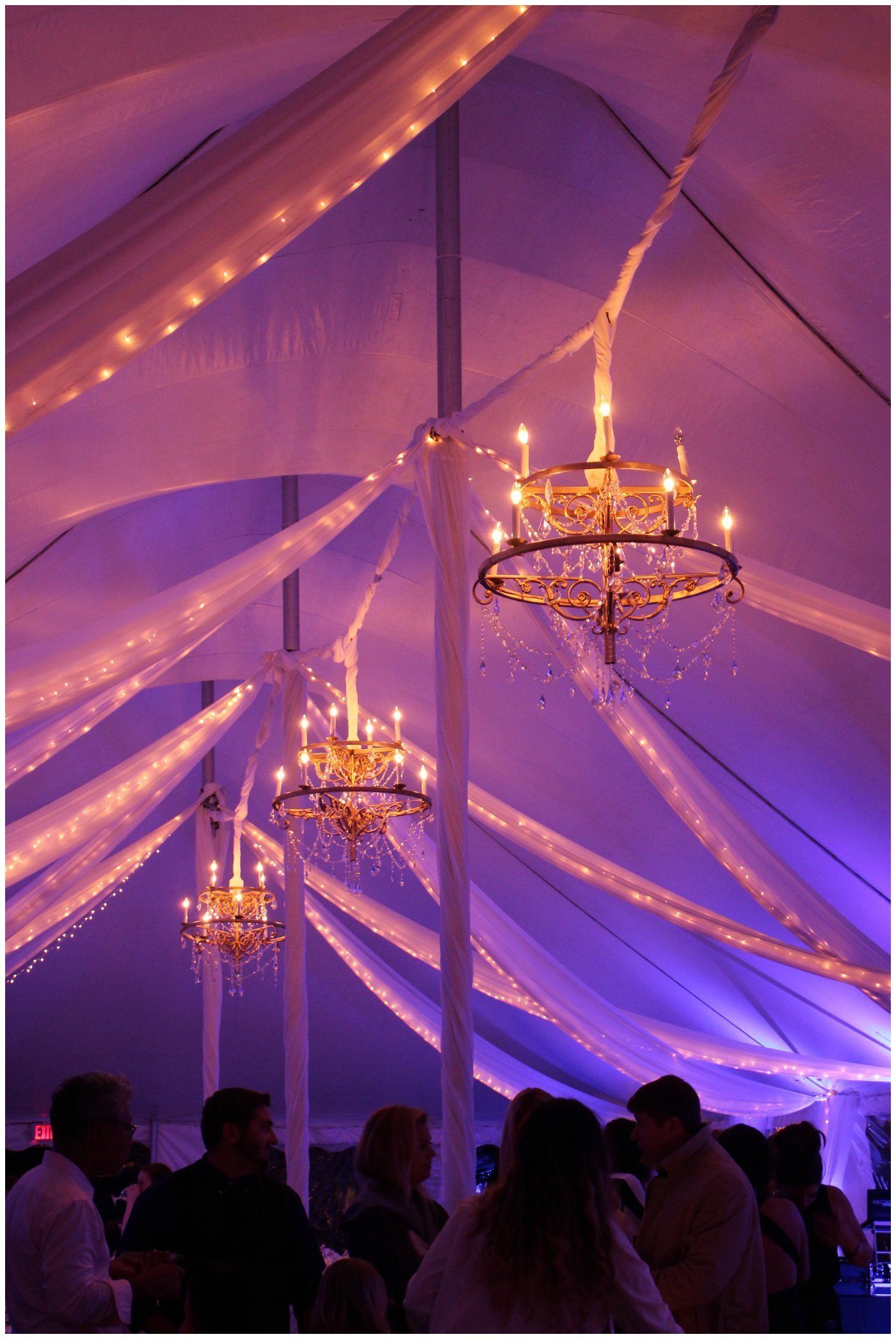 Purple-lit tent interior with hanging chandeliers and silhouetted guests below