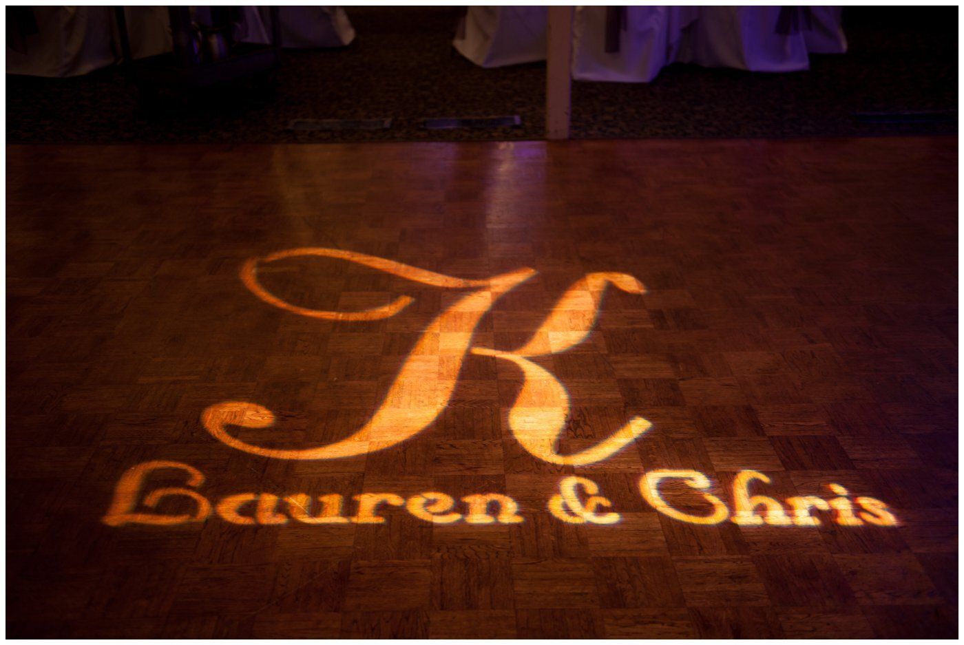 Projected gold monogram “K” with the names “Lauren & Chris” on a dark dance floor.